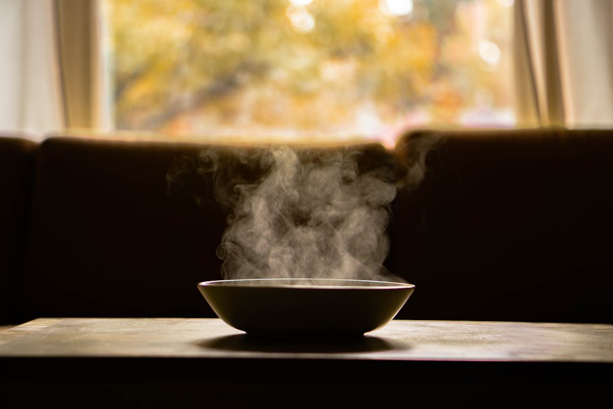 A single steaming bowl on a wooden table with soft window light in the background, warm-toned editorial composition. A metaphor for the daily work of a Chinese F&B owner.